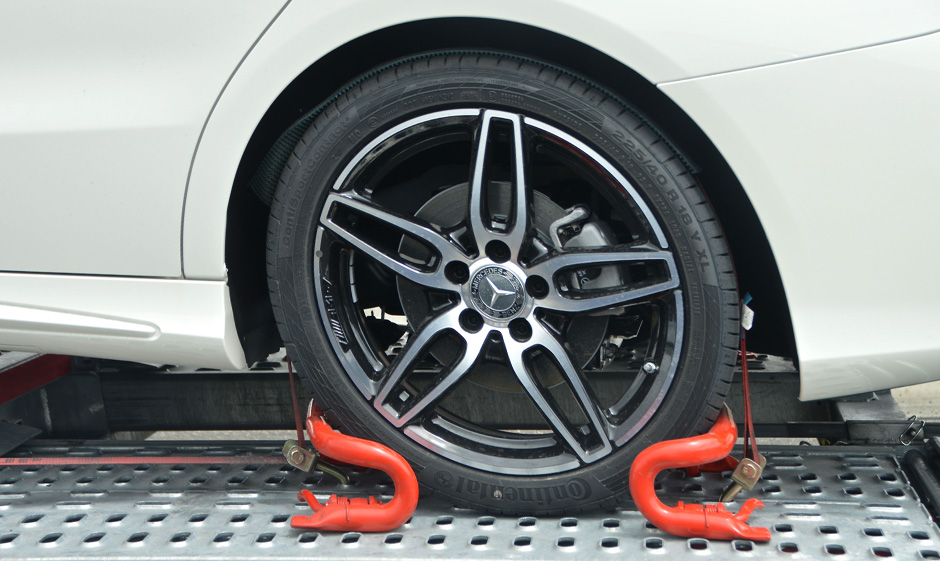 Photo of the wheel of the white car inter-locked in the flatbed towing truck surface